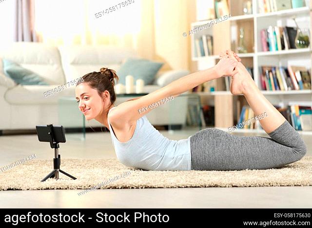 Profile of a happy woman doing yoga exercise watching video tutorial on smart phone at home