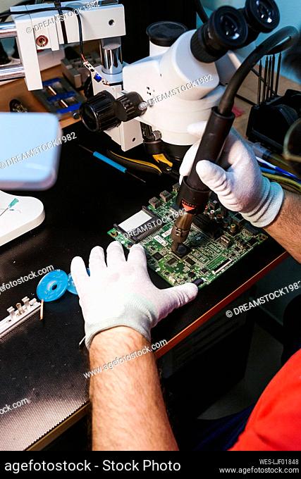 Repairman using blow torch on circuit board at workbench in workshop