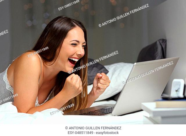 Excited woman winning online prize lying on the bed in the night at home