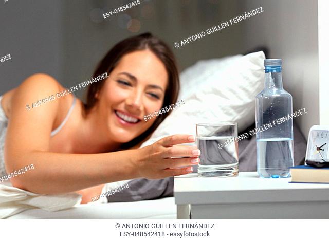 Happy thirsty girl catching a glass of water on the bed in the night at home