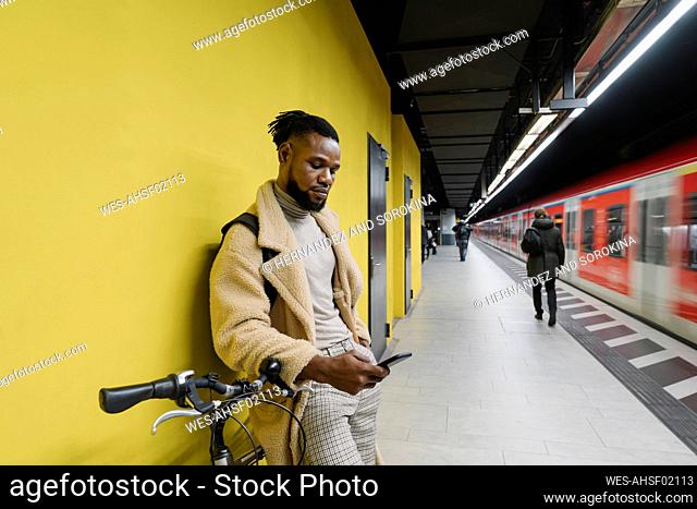 Stylish man with a bicycle and smartphone in a metro station