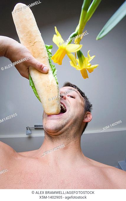 Man eating a large baguette in his kitchen