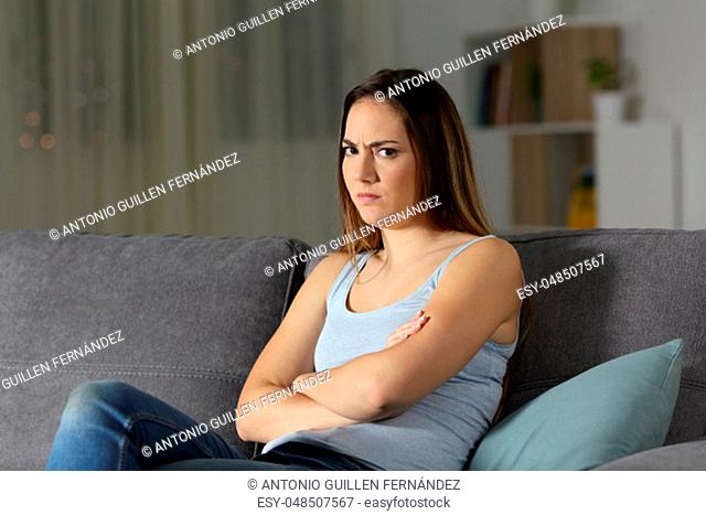 Angry woman looking at you in the night at home sitting on a couch in the living room at home