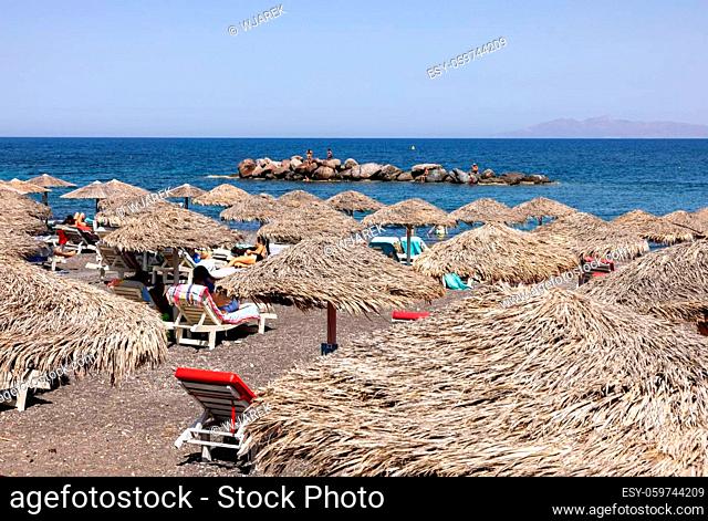Kamari, Santorini, Greece - June 27, 2021: Sun loungers on the black volcanic beach of Kamari in Santorini. Cyclades, Greece