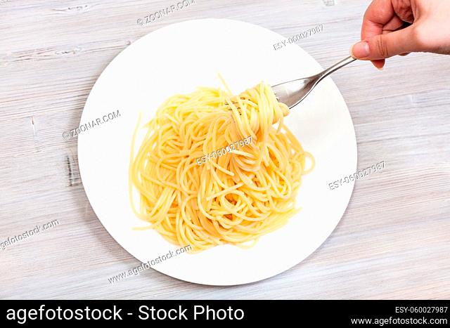 top view fork with strands of spaghetti al burro (pasta with butter) over white plate on gray wooden table