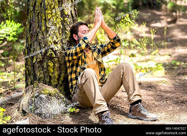 adult man in the forest sitting on the ground doing meditation and feel in love with woods outdoors nature around - concept of healthy lifestyle and happy...
