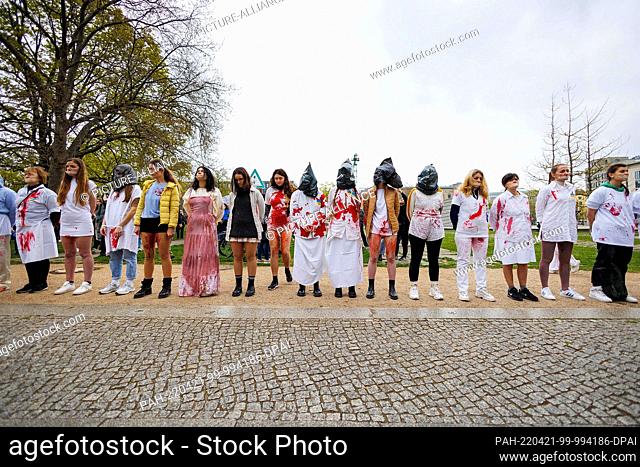 21 April 2022, Berlin: Women protest in front of the Federal Ministry of Economy in white clothes with artificial blood on them as well as joined hands during a...