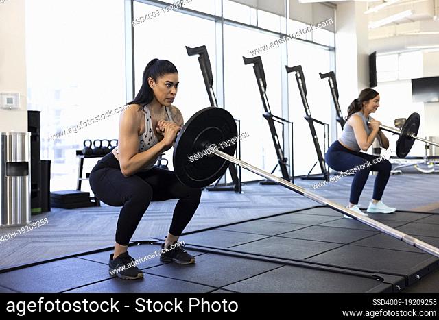 Woman taking a deep breath while doing barbell squats in gym