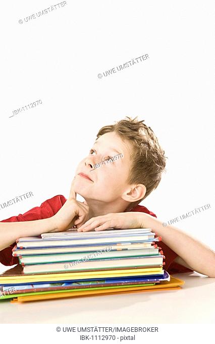Thoughtful looking boy sitting in front of a pile of exercise books and school books