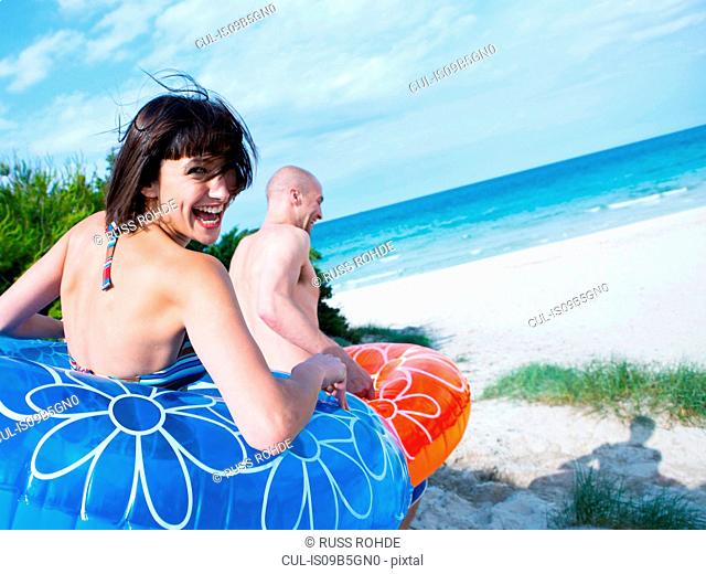 Couple in floats running down to the beach, Mallorca, Spain
