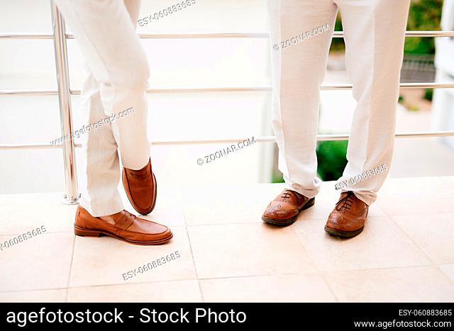 The legs of two men standing on the balcony, close-up. The groom and his best man during the preparation for the wedding ceremony