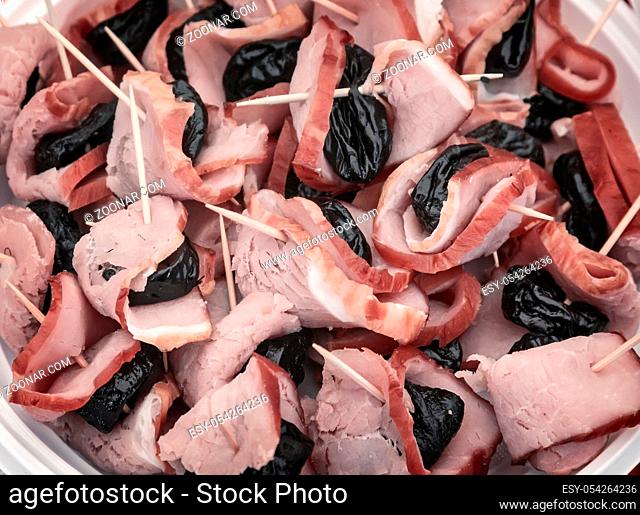 Appetizer of meat: slices of ham and prunes glued thin sticks. Presents closeup