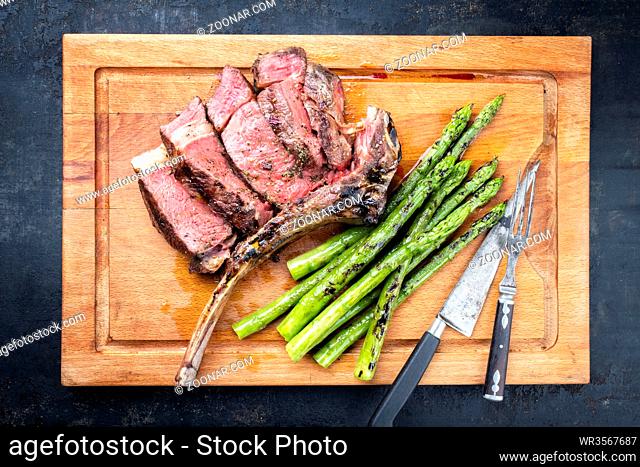 Barbecue dry aged wagyu tomahawk steak with green asparagus as top view on a wooden board