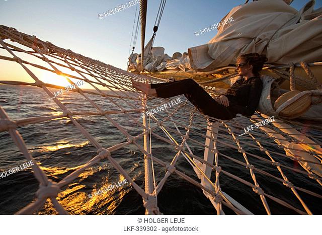 Woman relaxing in bowsprit net of sailing cruiseship Star Flyer Star Clippers Cruises at sunset, Pacific Ocean, near Costa Rica, Central America, America