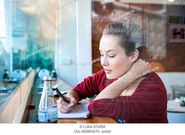 Young woman sitting in cafe, writing in notepad