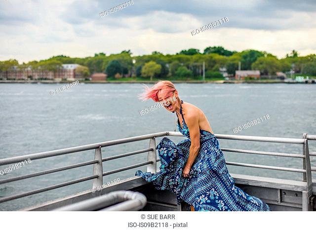 Mature woman standing on boat, laughing, wind blowing dress
