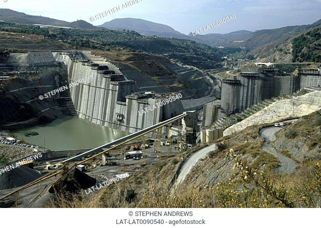 The construction of a dam in the River Guadalfeo valley with terraced slopes and concrete panels being placed on slopes, a water reservoir in the making