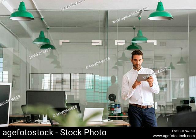 Focused young businessman using a digital tablet while working alone in a large modern office