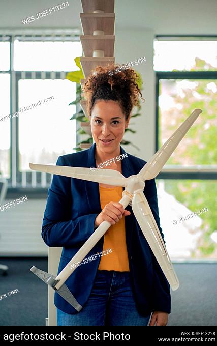 Confident businesswoman with wind turbine model standing in workplace