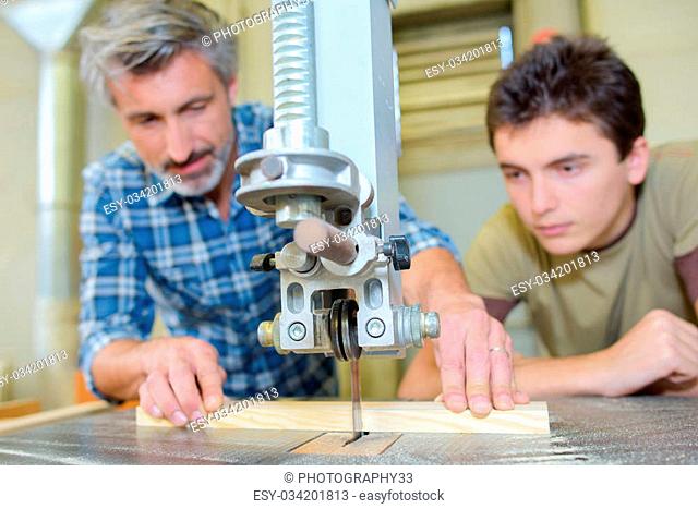 Carpenter teaching apprentice to use a bench saw