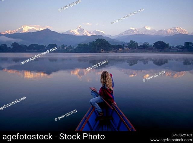 A woman in a rowboat gazes at the Annapurna Range at dawn.; Annapurna Range, Himalaya Mountains, Nepal