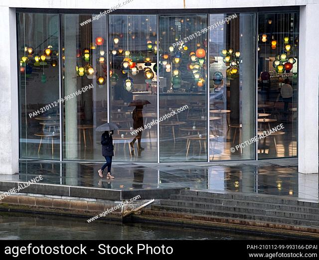 12 January 2021, Berlin: A woman walks past the Bundestag restaurant on the banks of the Spree river, where tables without chairs are standing around