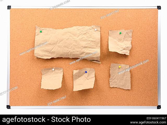 cork board with aluminum frame and brown paper pieces attached, board isolated on white background