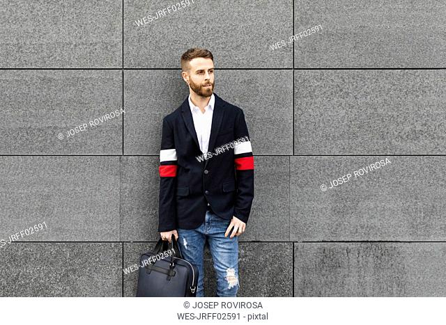 Stylish businessman standing in front of grey wall looking around