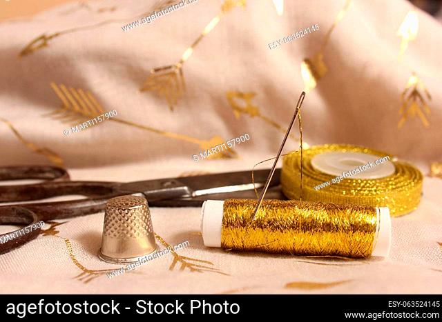 Spool of Gold Thread and Scissors With Thimble on Metallic Chiffon Fabric