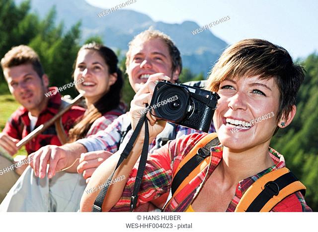 Austria, Salzburg County, Men and women sitting in alpine meadow, woman holding camera