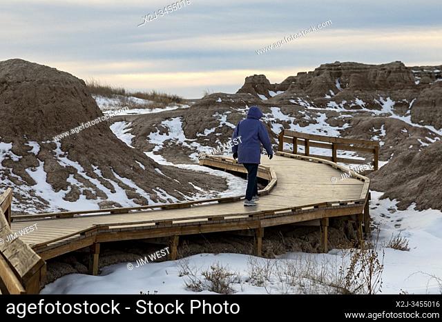 Badlands National Park in winter. A visitor walks on a boardwalk, part of the Fossil Exhibit Trail