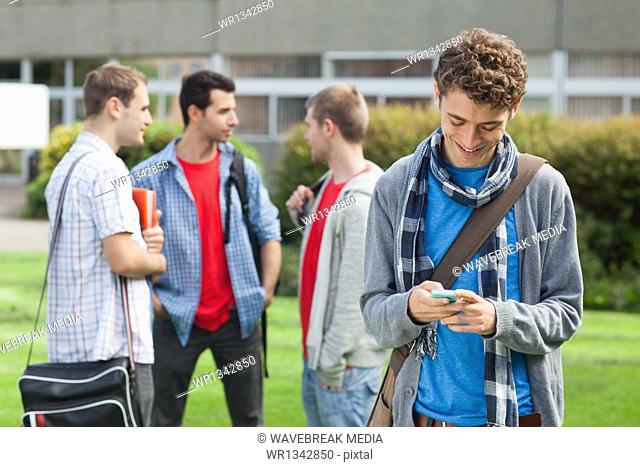 Happy male student sending a text in front of his classmates outside
