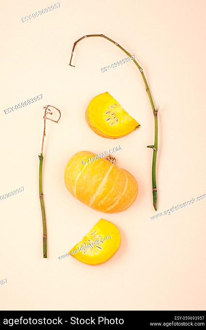 Fresh orange cut pumpkin and dried branches on a light beige pastel background close-up