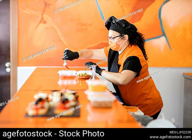 Female chef wearing protective face mask packing food in container at cafeteria