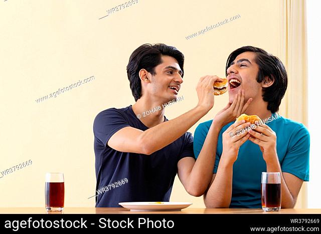 Portrait of teenage boy feeding hamburger to his friend
