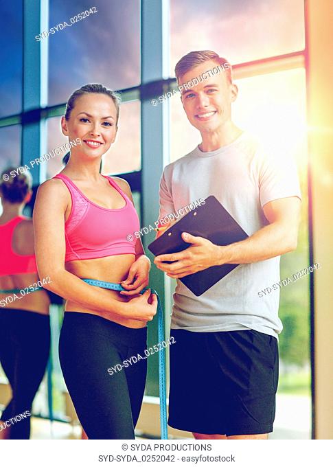 smiling young woman with personal trainer in gym