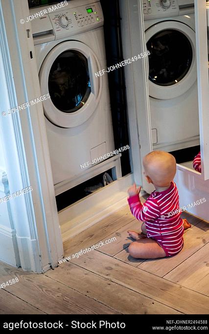 Baby girl sitting in front of washing machine