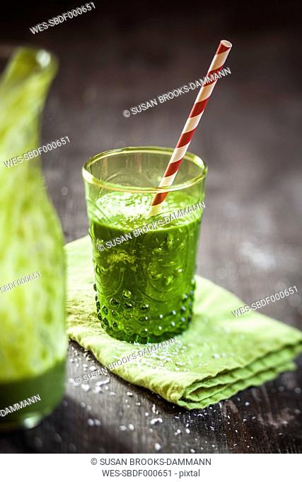 Glass of spinach smoothie with coconut milk, lemon- and orange juice and banana on napkin and wooden table