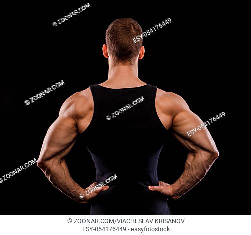 Portrait of a muscular male model against black background. Personal trainer. Black t-shirt. Back view