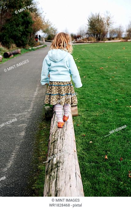 View from behind of a four year old girl walking and balancing on a log