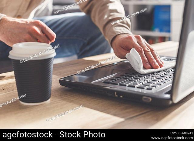 Man disinfects his laptop, cleaning keyboard . Wipe with rubbing alcohol spray and disinfectant