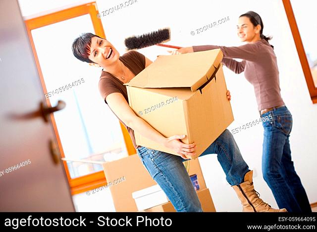 Young women lifting up cardboard box and having fun, while moving to new home