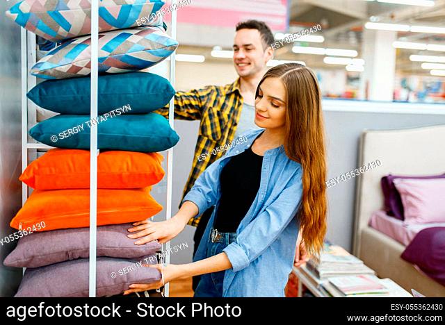 Young love couple holds pillows in furniture store. Man and woman looking samples for bedroom in shop, husband and wife buys goods for modern home interior