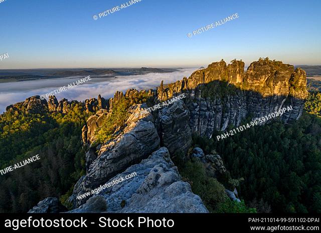 10 October 2021, Saxony, Bad Schandau: View from the Schrammstein lookout in Saxon Switzerland of the rocks of the Schrammsteine and the fog passing by in the...