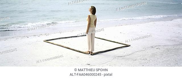 Woman standing in corner of square outlined on beach by lengths of bamboo