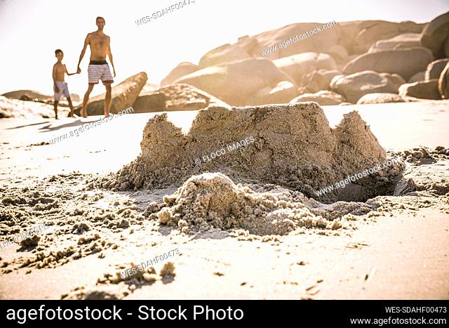 Sand castle on the beach with father and son walking in background