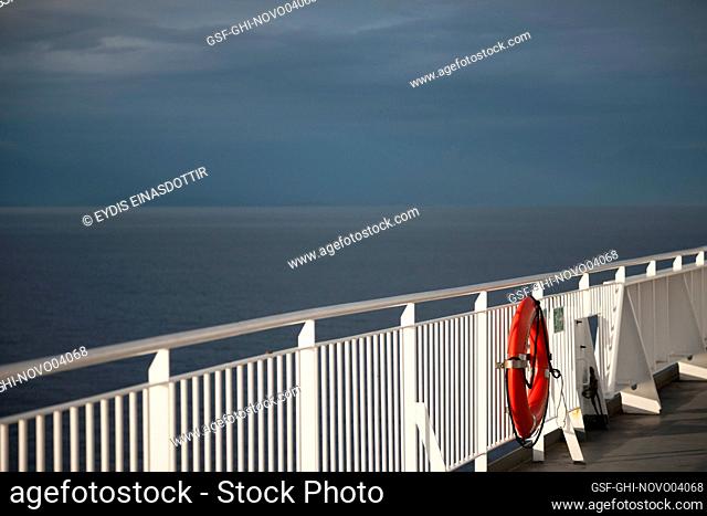 Ferry railing with lifebuoy ring against a dramatic sky and dark ocean