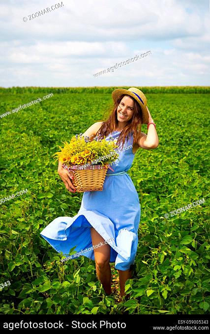 girl in a hat stands on a green field with a basket of flowers
