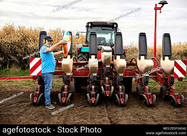 Male farmer wearing ear protectors while pouring corn in containers of tractor at agricultural field