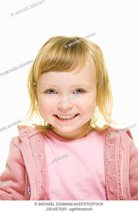 A three year old girl with blonde hair wearing a pink sweater and a pink top looks into camera with a big smile